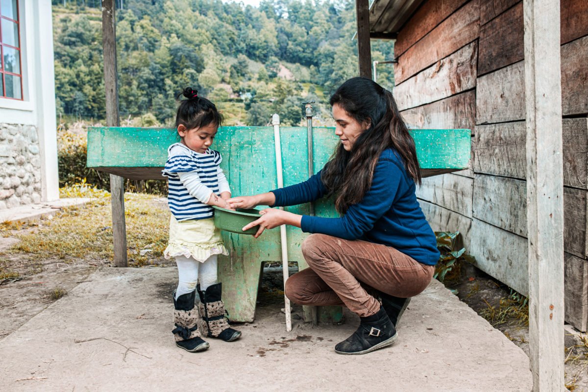 A woman washes the hands of her daughter in Guatemala.