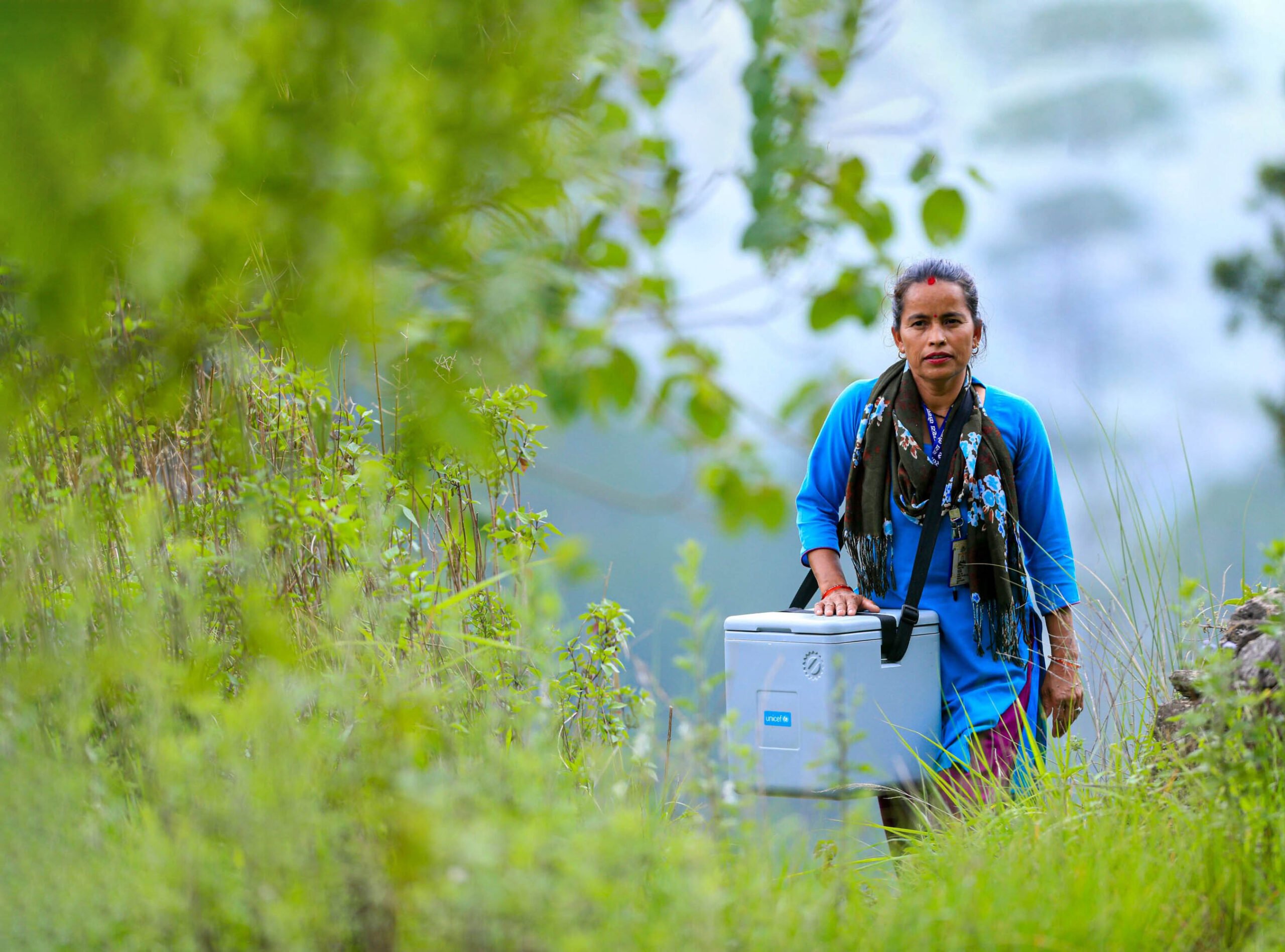 Health worker carrying a cooler box of vaccines en route to a community outreach vaccination session.